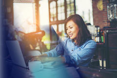 An Asian woman working on her laptop with a cup of coffee next to her.